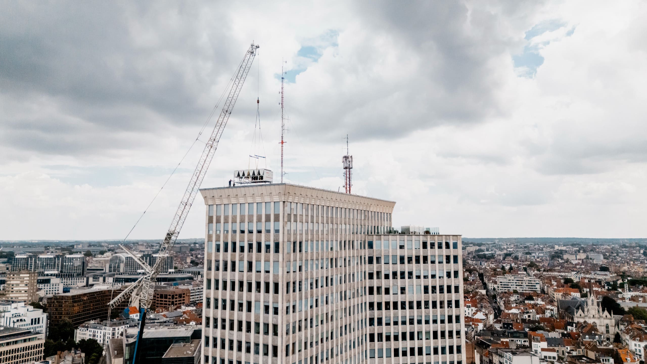La tour sous un ciel chargé, la grue et ses câbles tendus vers le toit.