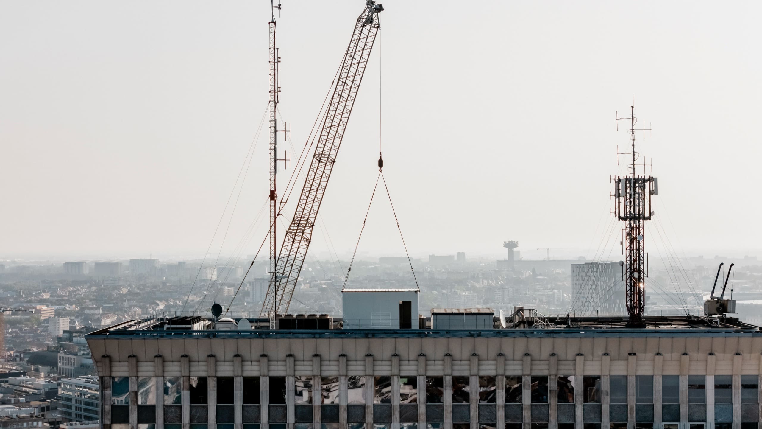 Au sommet de la tour, une pièce suspendue à la grue arrive au-dessus du toit, entre les antennes.