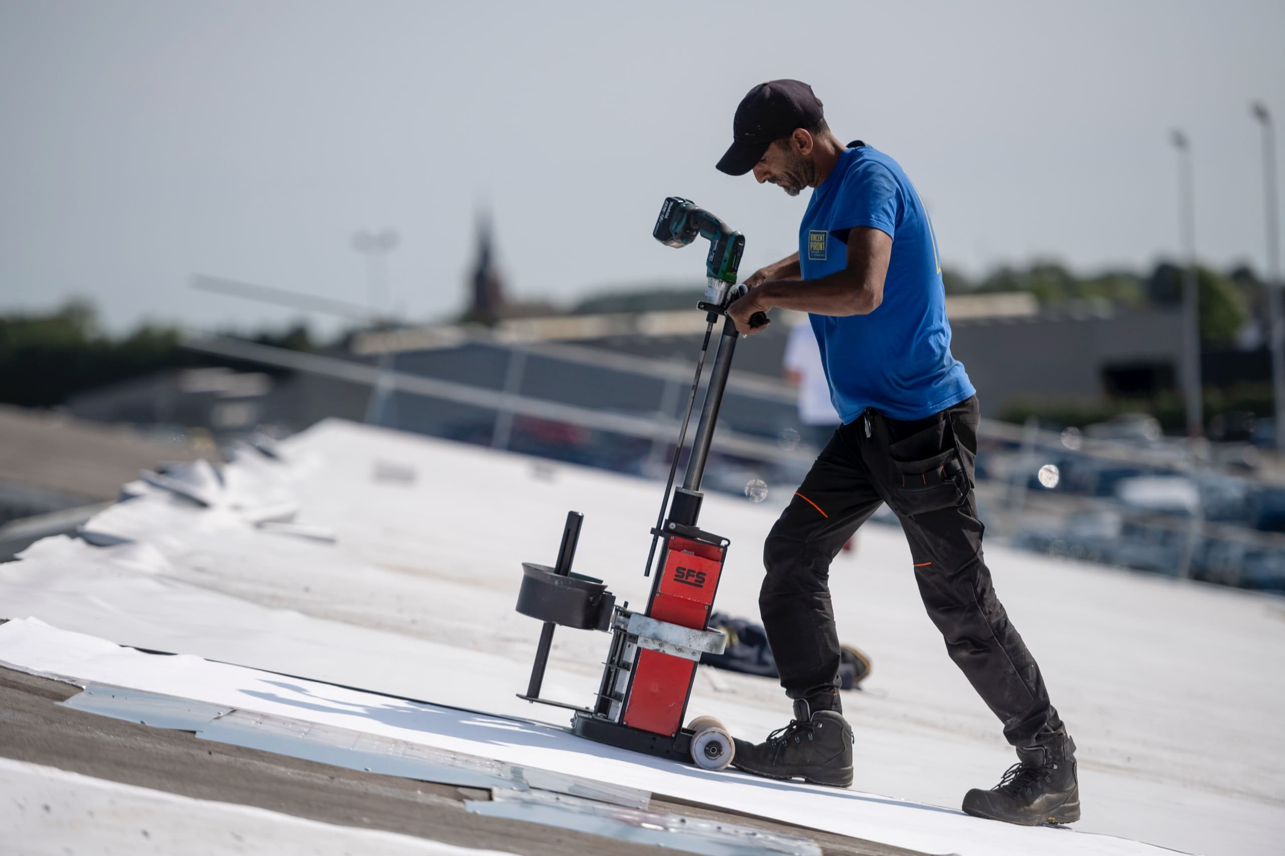 Un couvreur pousse une soudeuse automatique sur une membrane de toiture blanche.