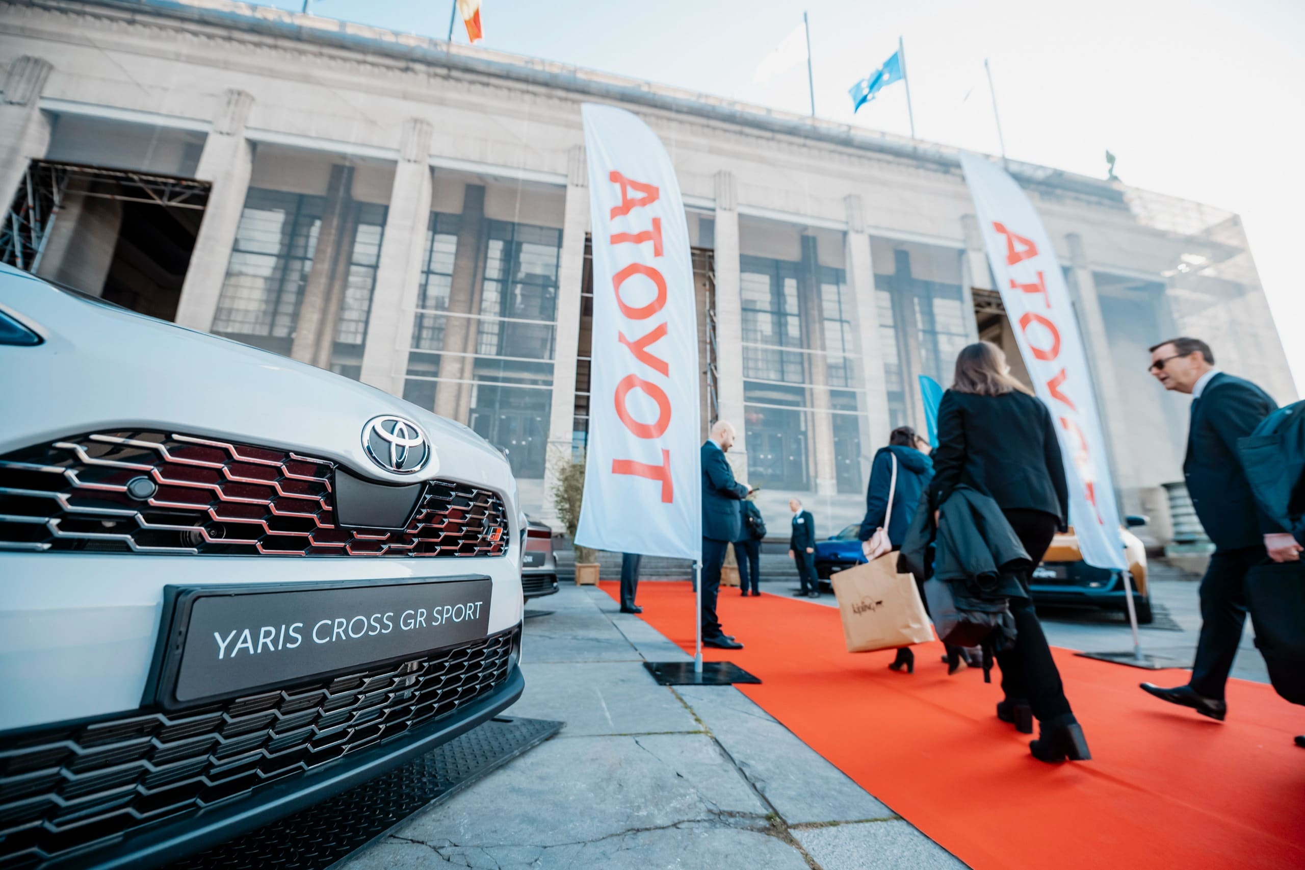 À l’entrée, une voiture exposée et le tapis rouge ; les invités arrivent avec leur valise.