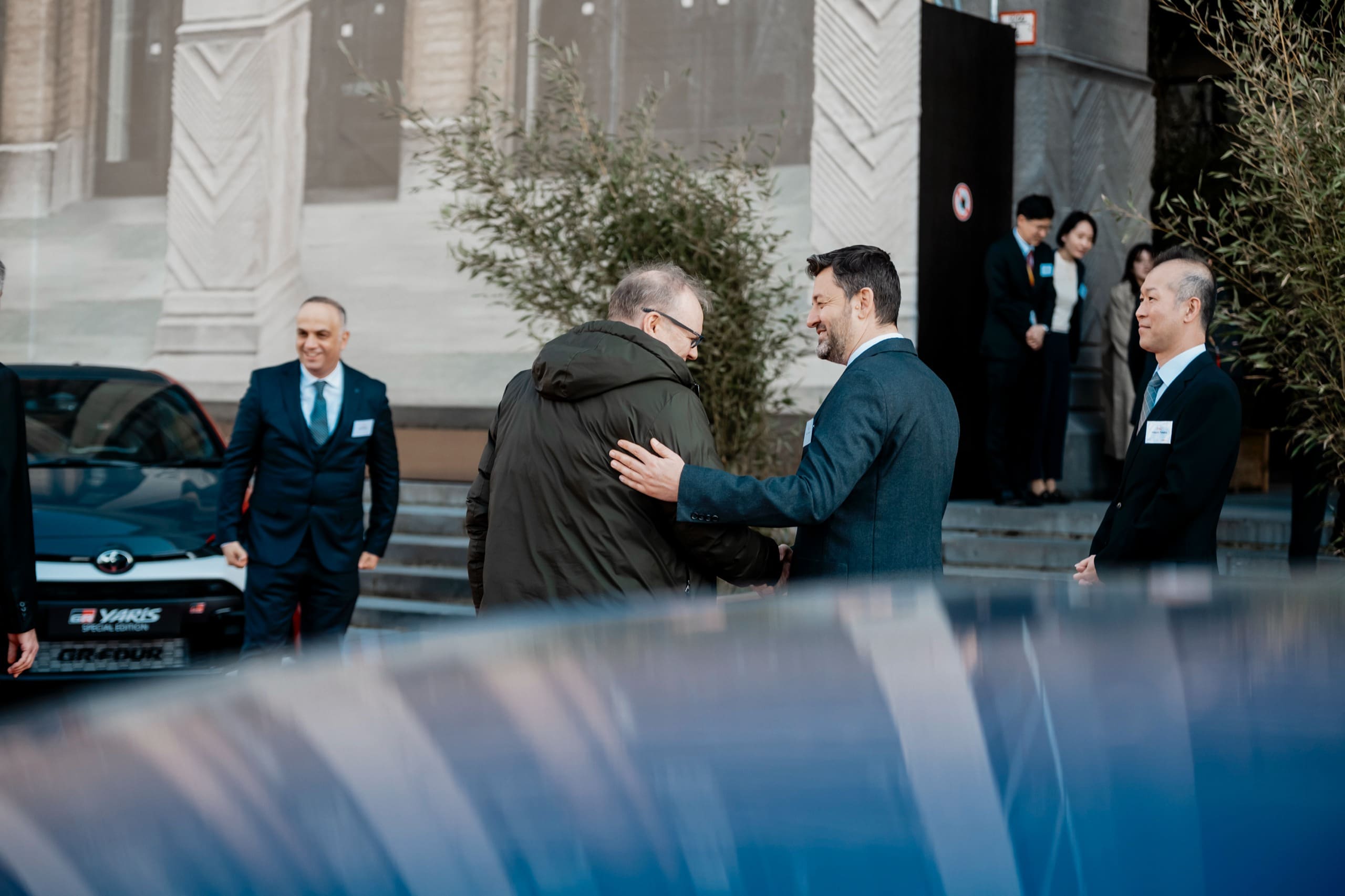 Accueil devant l’entrée : poignée de main entre deux invités en costume.
