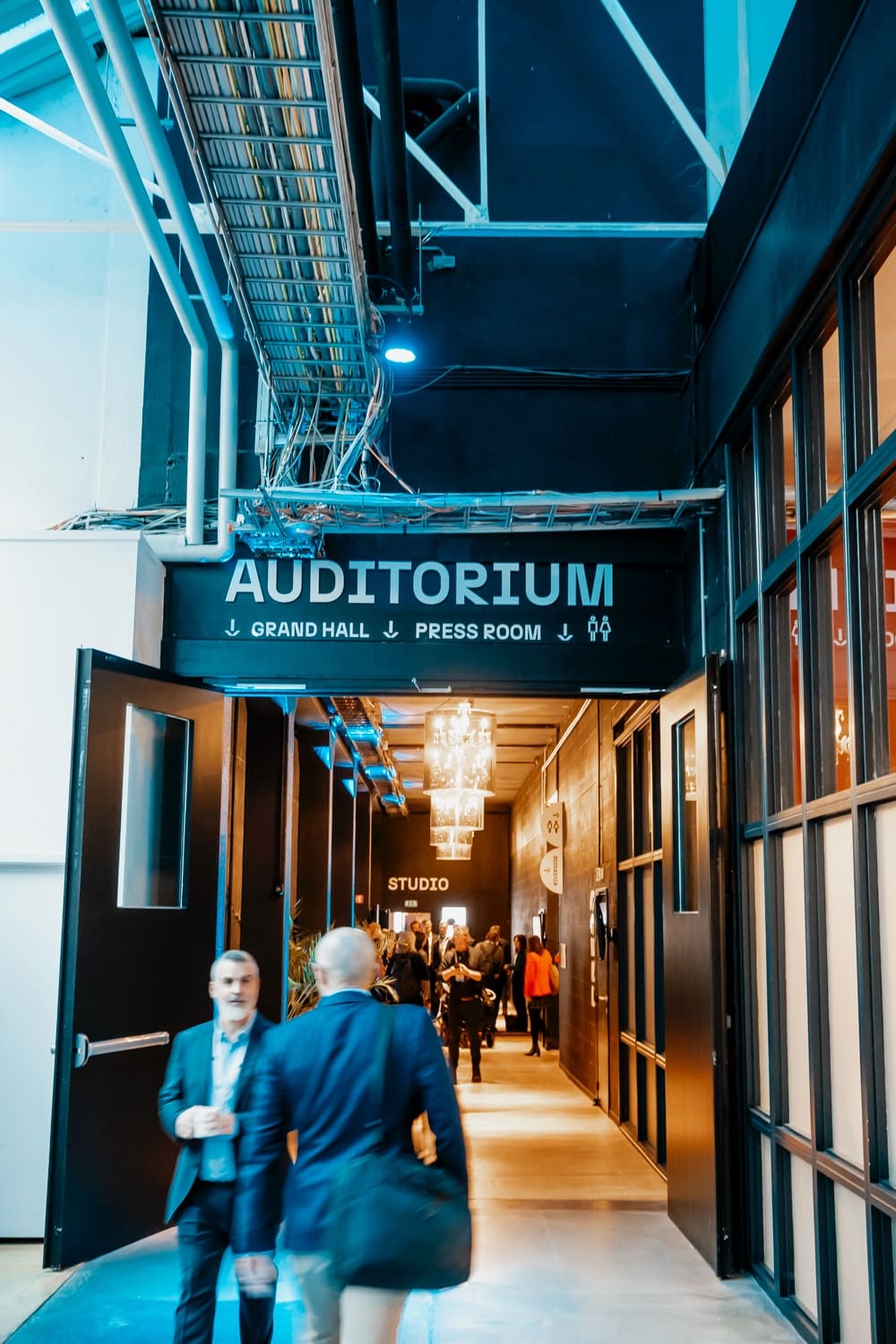 Entrance corridor of an auditorium under a chandelier, two participants on the move.