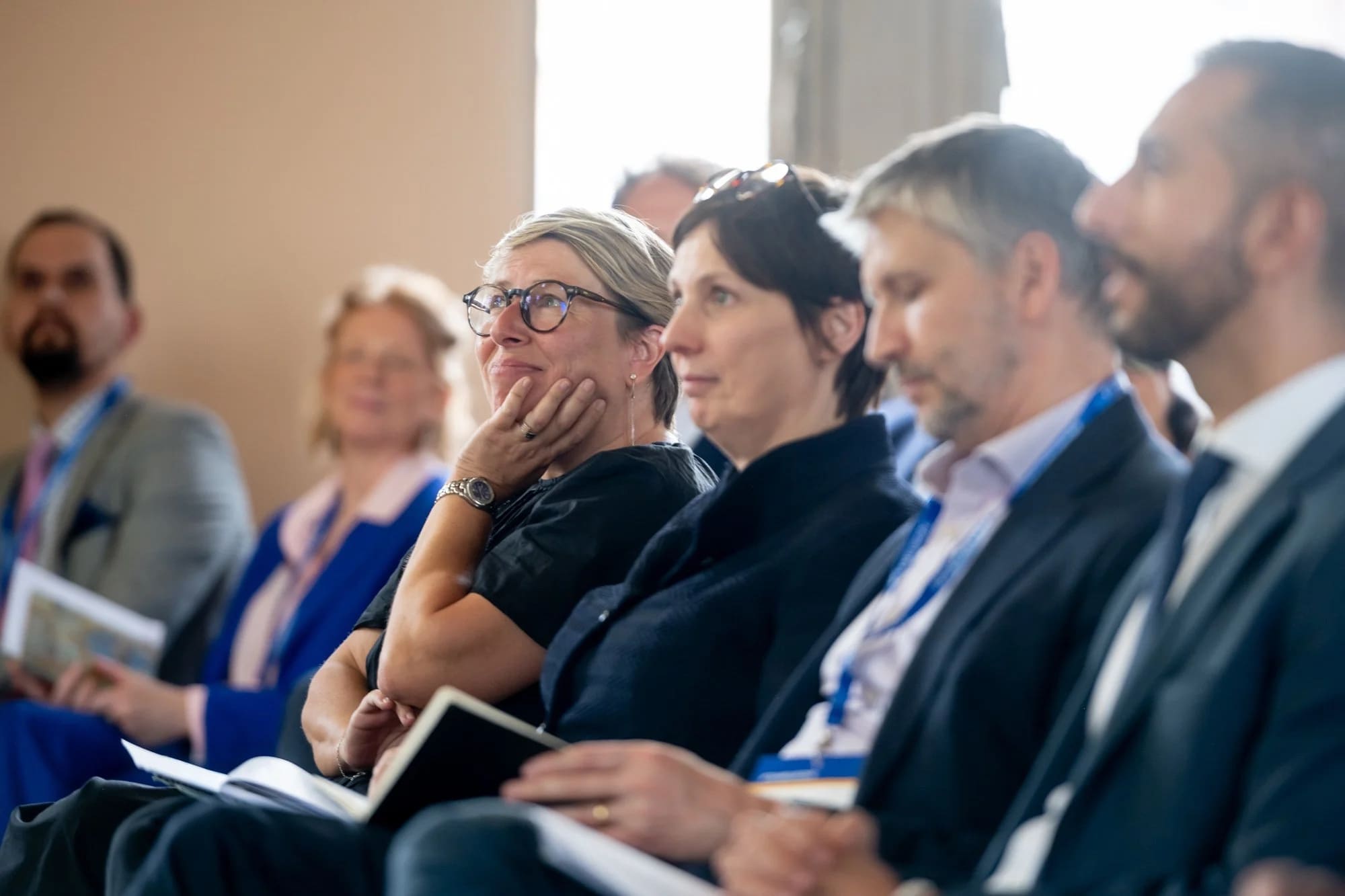 Attentive, smiling participants in the front row of a conference, notebooks in hand.
