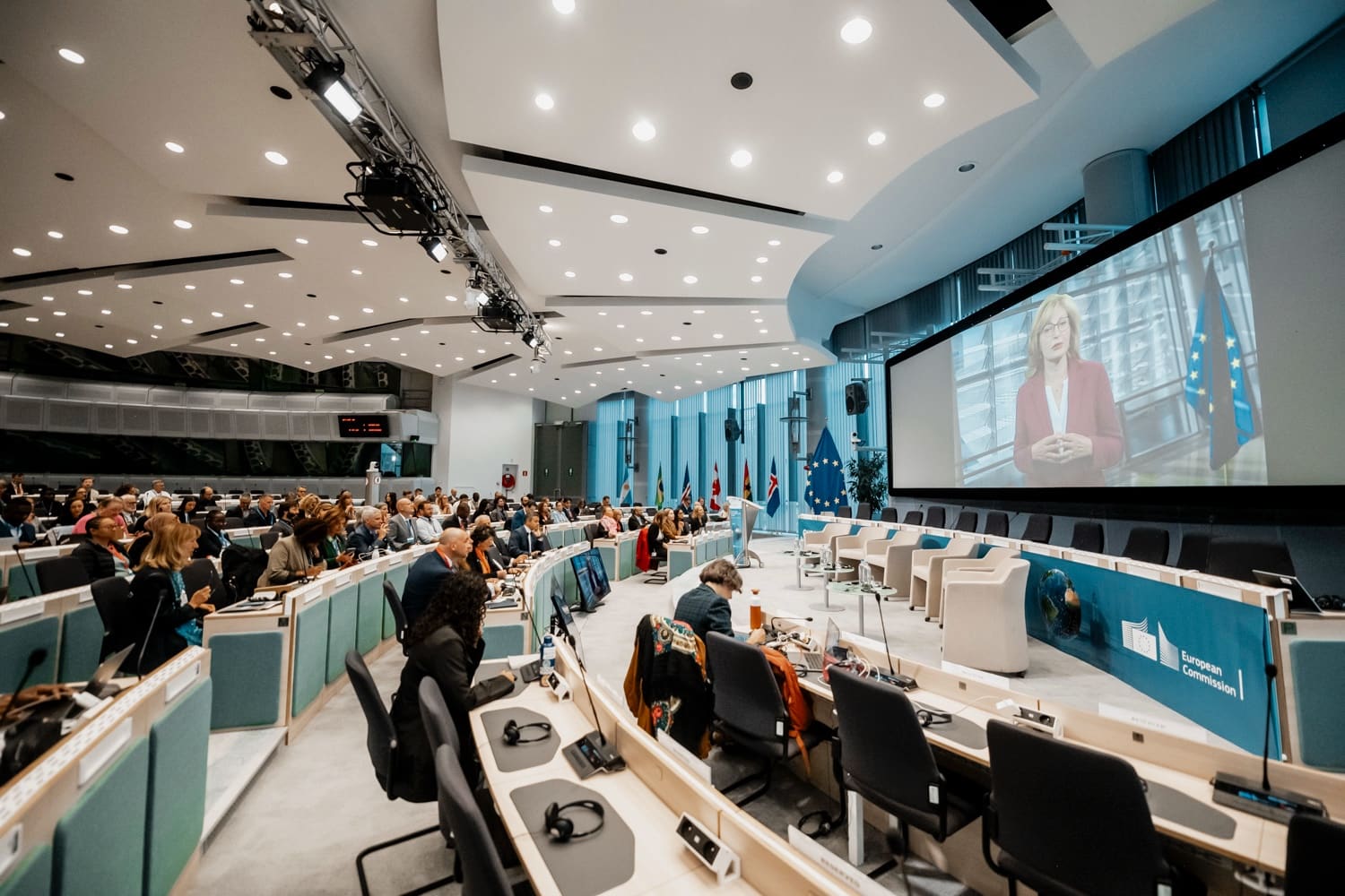 Large conference room: delegation desks with headsets, flags and a giant screen.