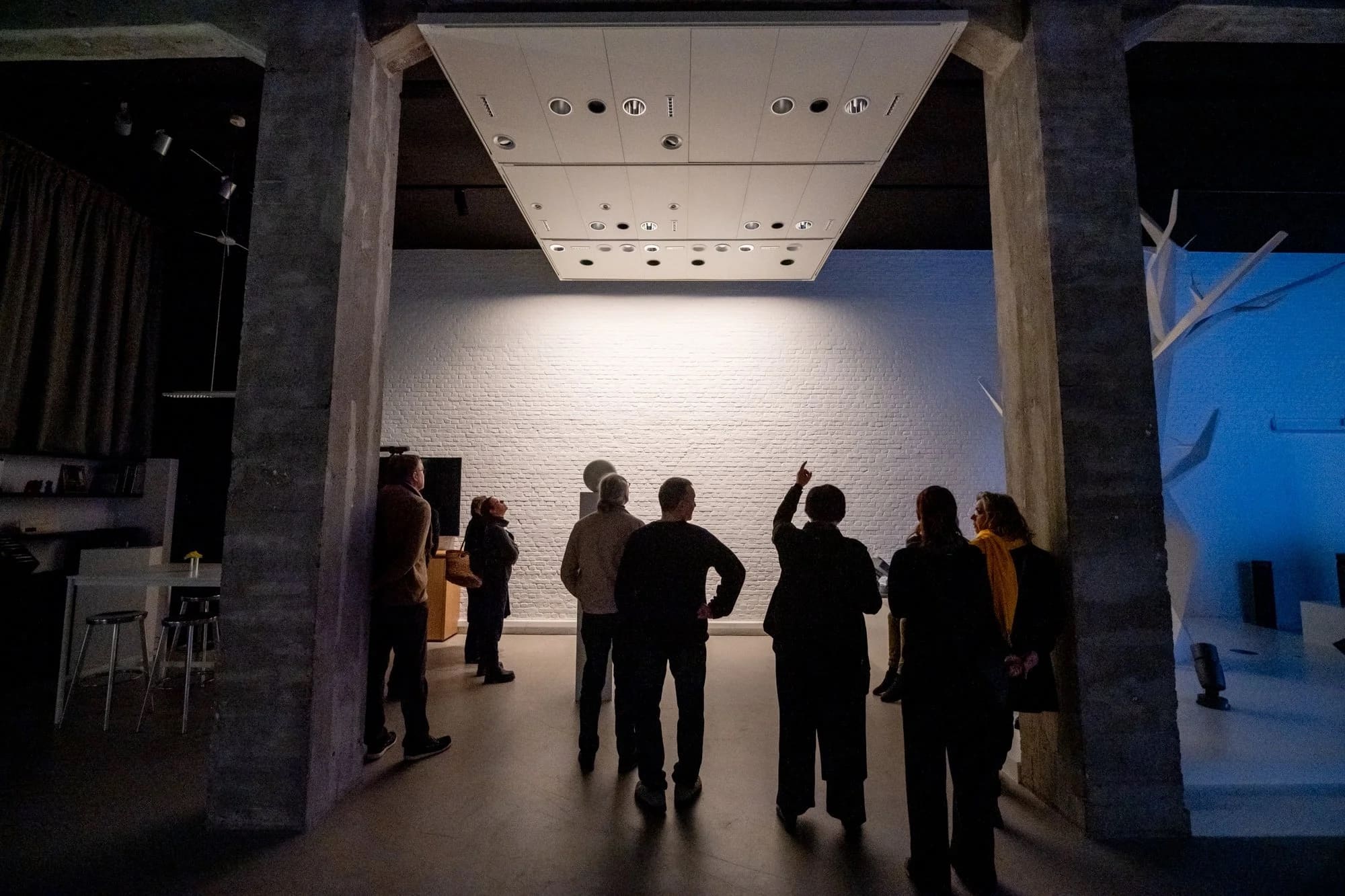 Bezoekers in silhouet onder een demonstratieplafond voor verlichting, witte bakstenen muren.
