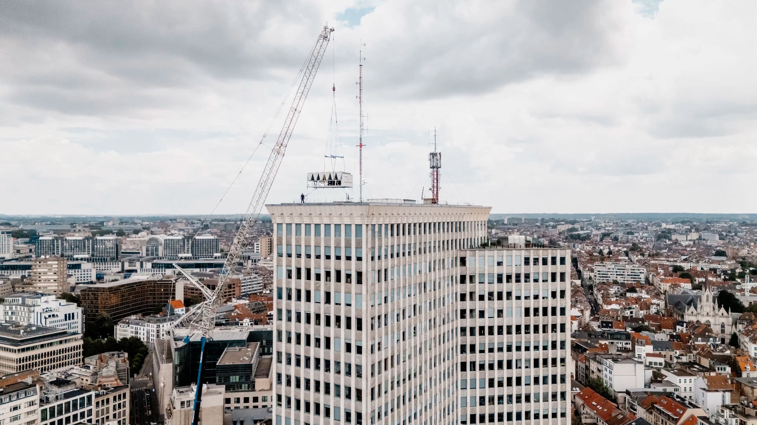 Aerial view of an office tower, a crane lifting technical equipment onto the roof.