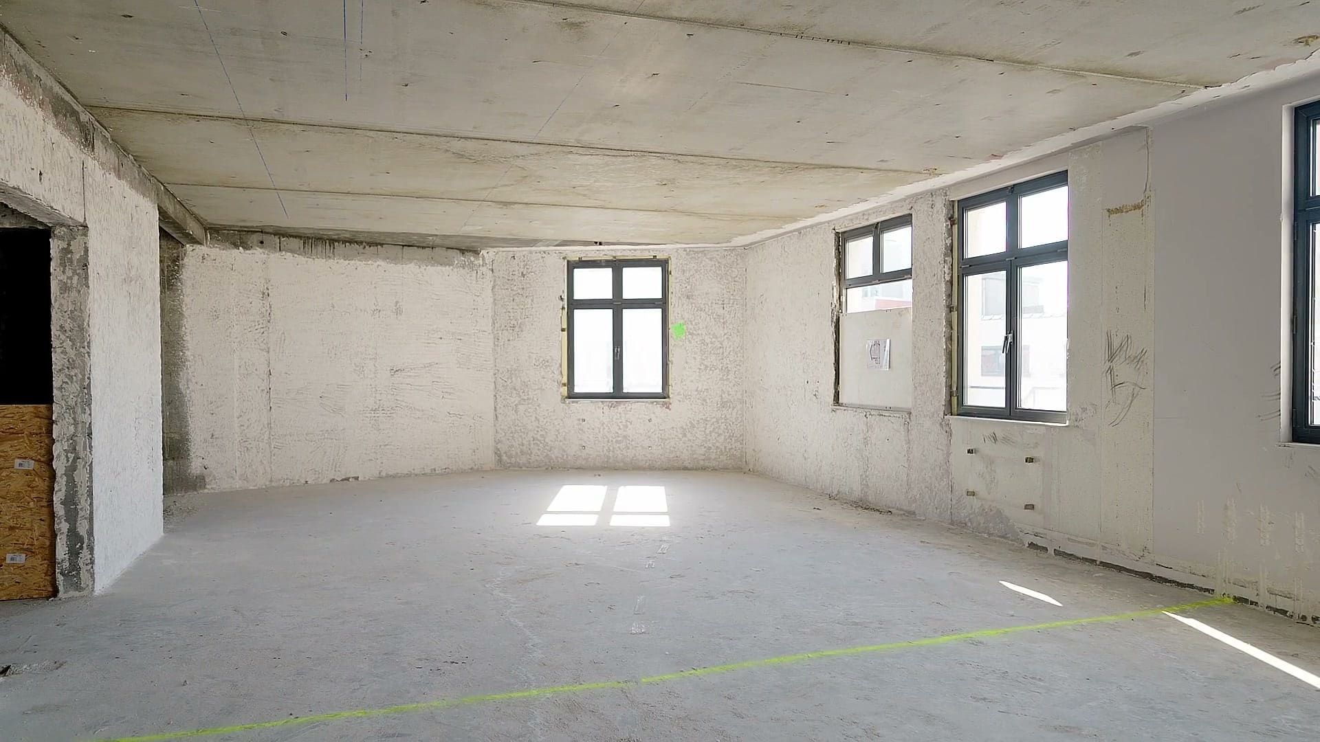 Un plateau vide, murs bruts et sol en chape, la lumière du jour entrant par les fenêtres.