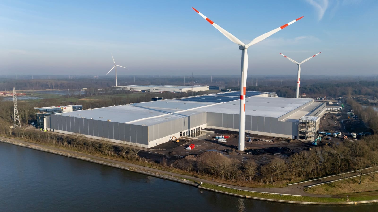 Groot nieuw logistiek magazijn aan een kanaal, windmolen op de voorgrond.