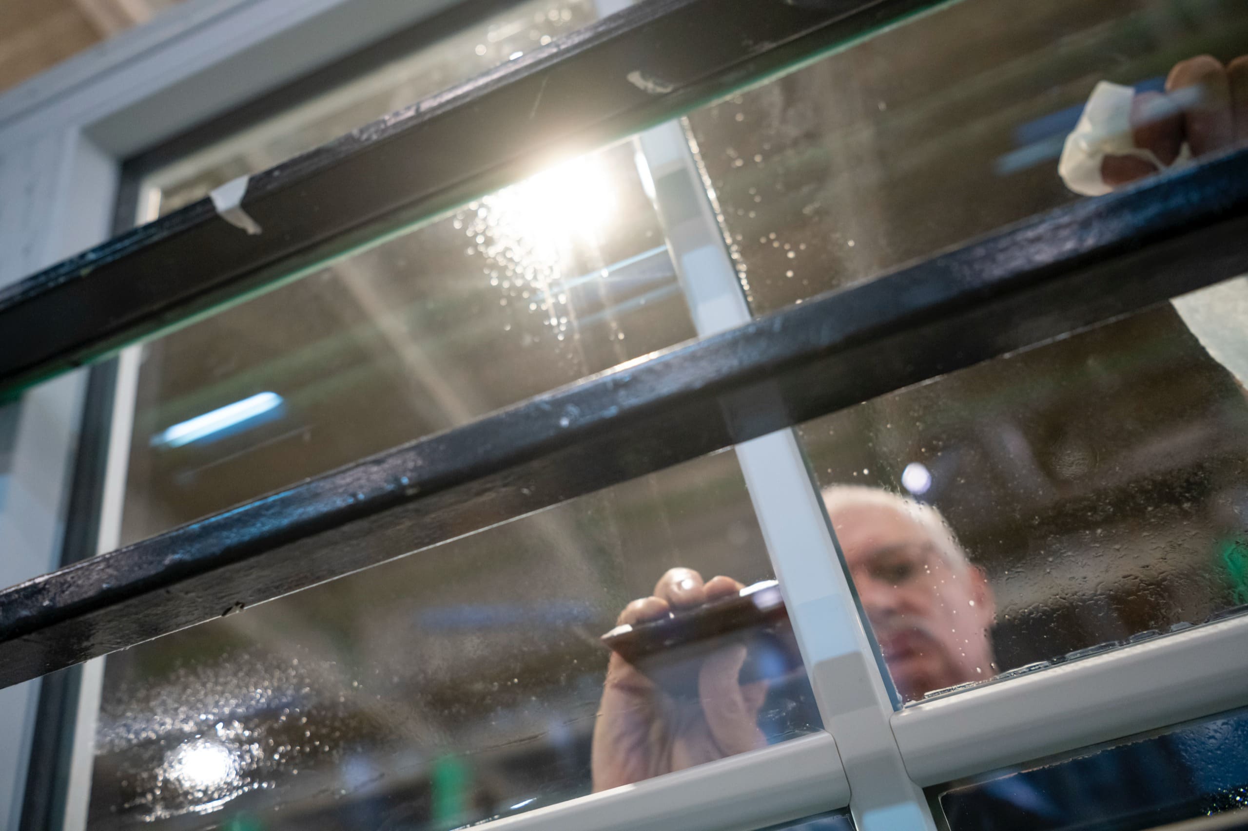 Le reflet d’un ouvrier dans une vitre, à travers les croisillons d’un châssis.