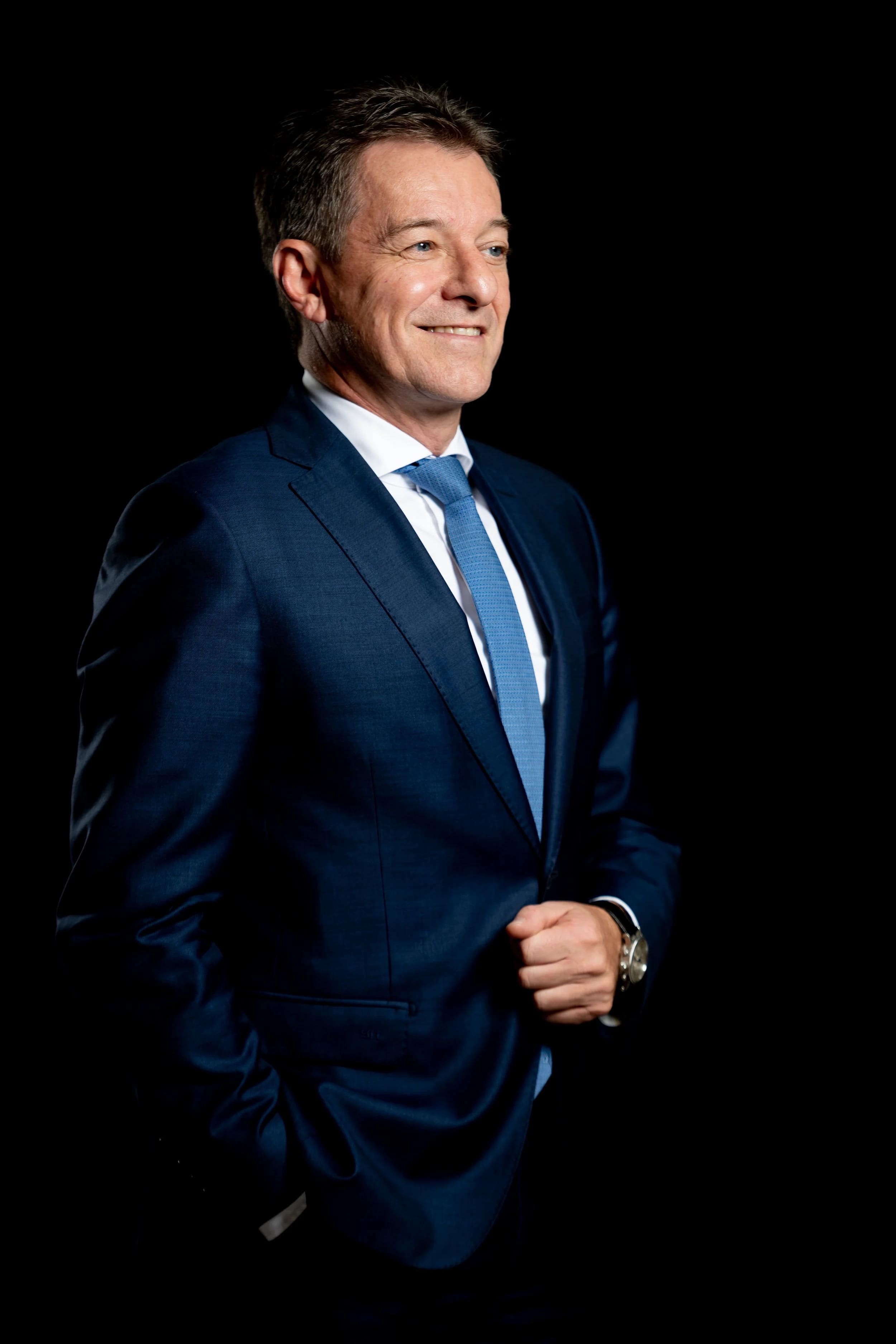 Portrait of a smiling executive in a navy suit, against a black background.